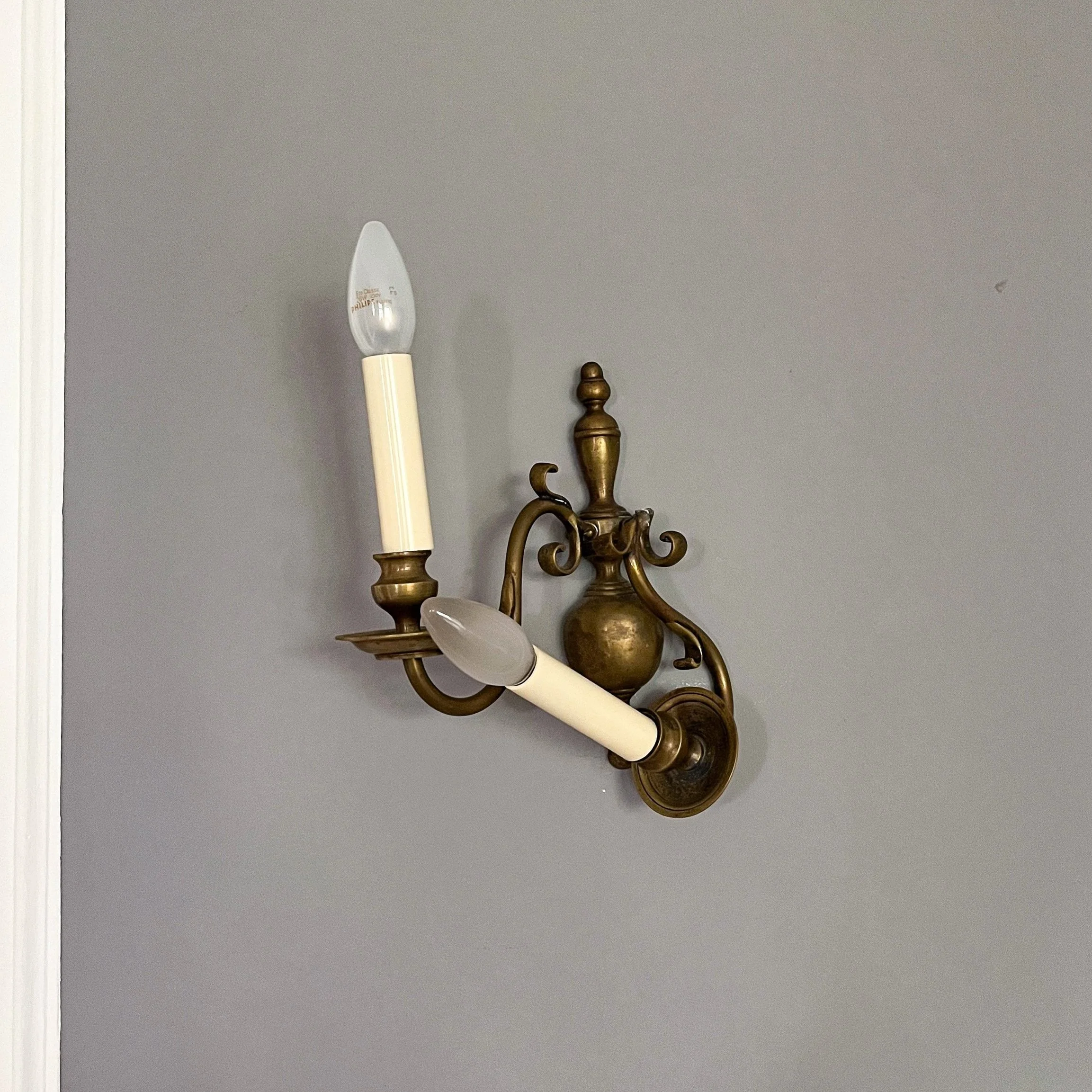 Nahaufnahme einer zweiflammigen Wandleuchte aus Messing an einer grauen Wand.