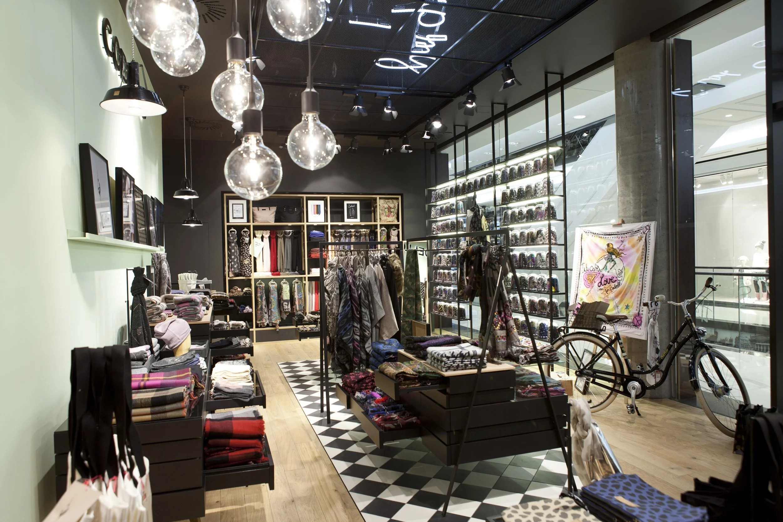 Der Codello Store in Berlin wurde mit Stahlregalen und herabhängenden Glühbirnen ausgestattet. Eine mintgrüne Wand bildet einen hellen Kontrast zu den Stahlregalen.