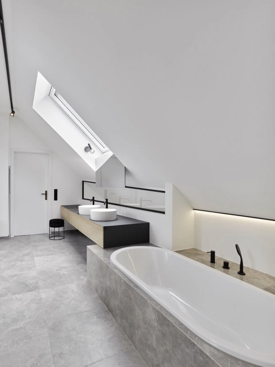 Modernes Badezimmer unter der Dachschräge mit Dachfenster, doppelter Waschtischkonsole, eingelassener Badewanne und mattschwarzen Armaturen.