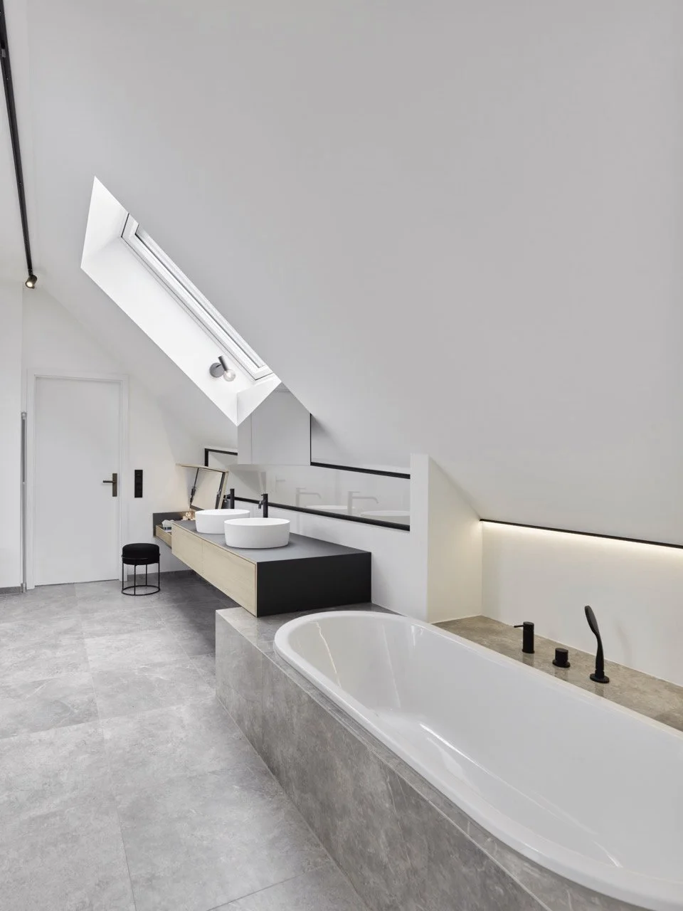 Vollständige Ansicht des Dachgeschoss-Badezimmers mit grauen Fliesen, heller Dachschräge, Badewanne und Blick auf die Eingangstür im Projekt K7.