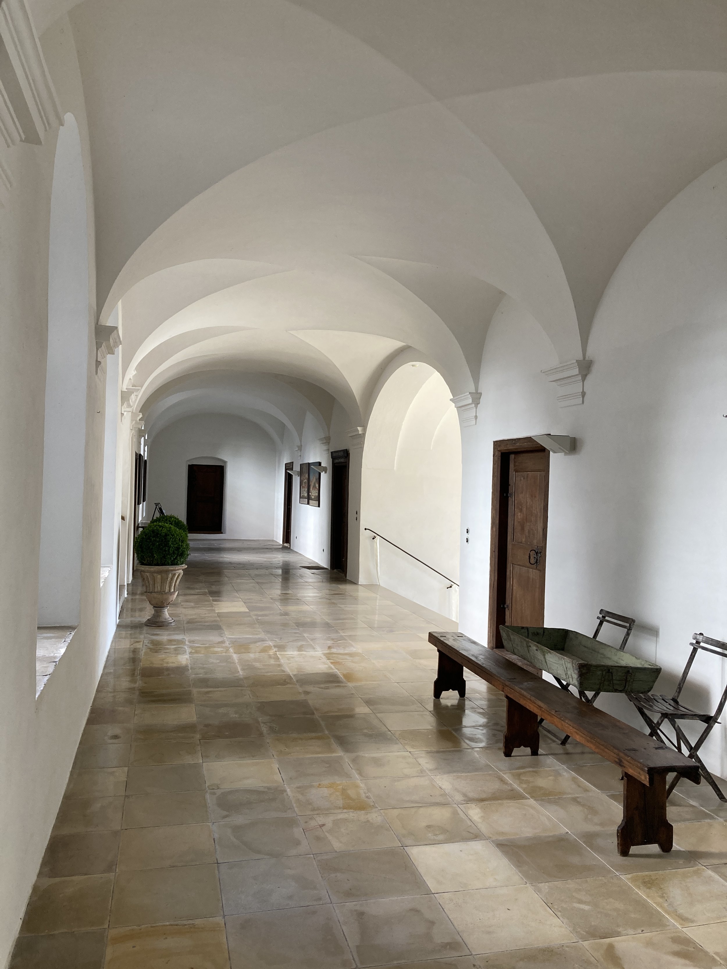 Neuer Schlossgang mit historischem Kreuzgratgewölbe, hellen Putzwänden, Natursteinboden, Massivholztüren und einfacher Holzbank.