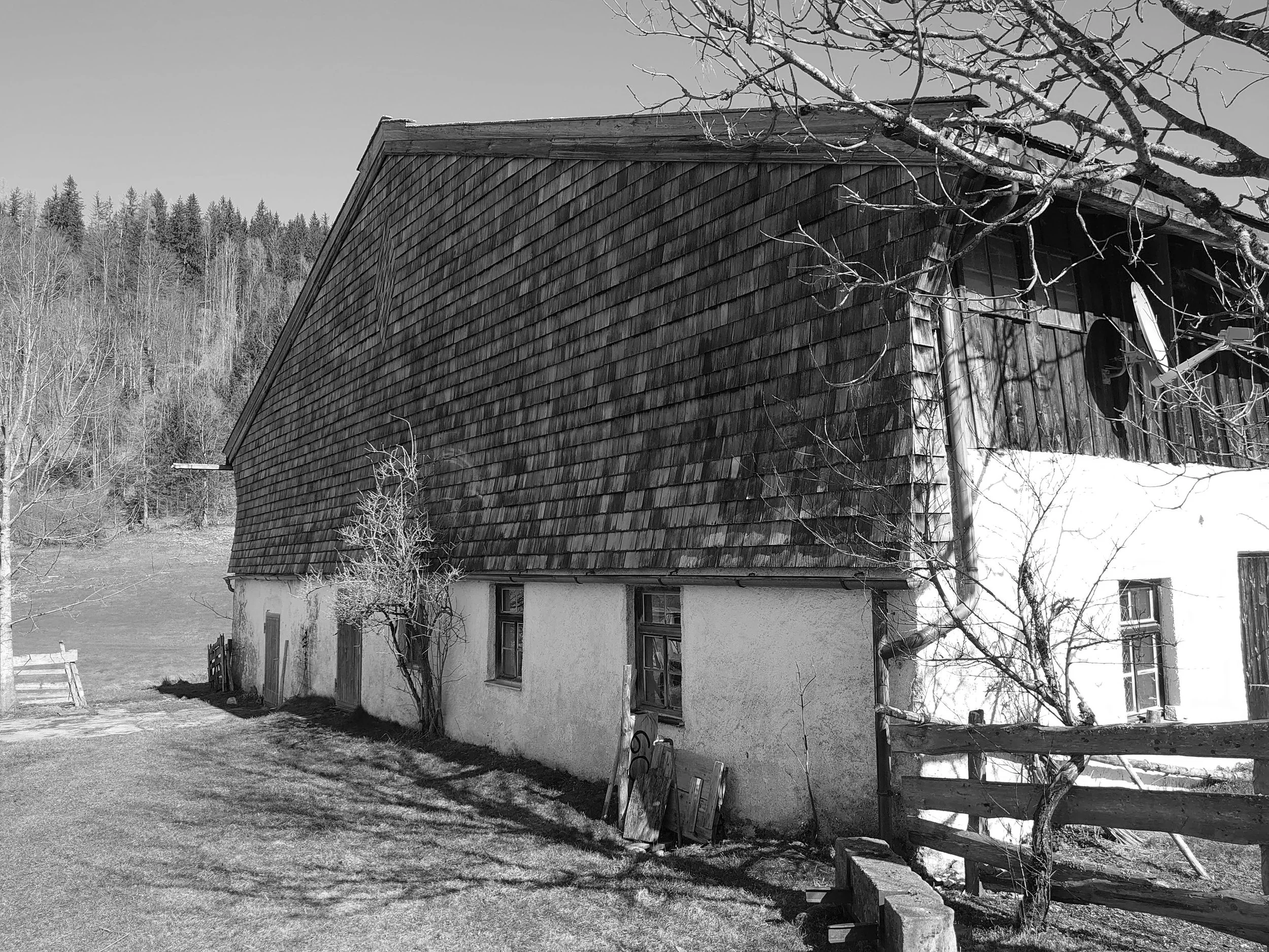 Aufnahme der Rückseite eines historischen Einfirsthofs mit schindelverkleidetem Obergeschoss, weiß verputztem Erdgeschoss und Holzzaun vor der Sanierung.