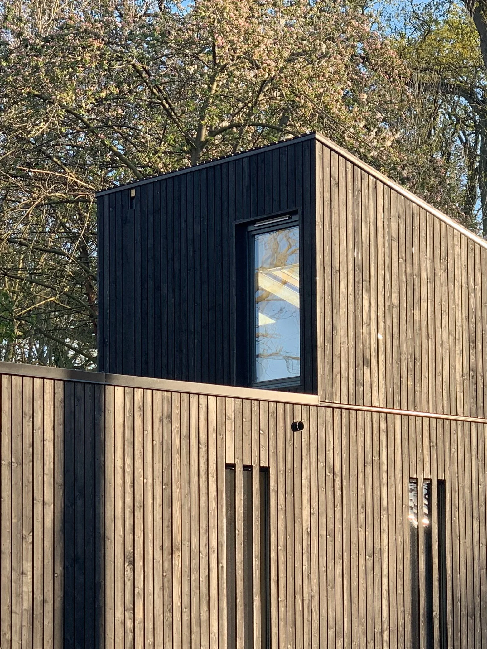Nahaufnahme eines Modulhauses mit vertikaler, dunkler Holzschalung, schmalen Fensterschlitzen und Oberlicht im versetzten Dachaufbau.