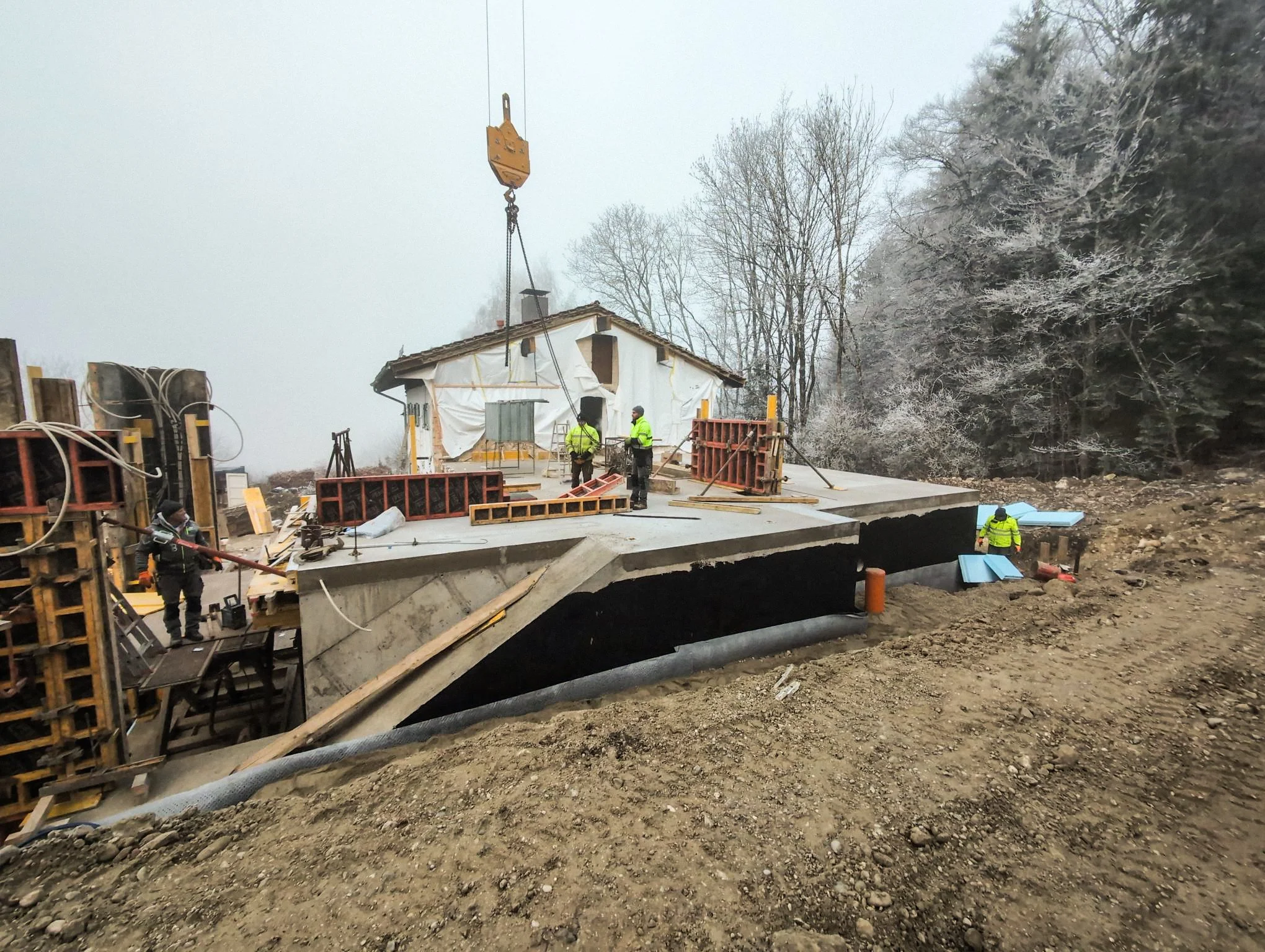 Baustelle von einem modernen Anbau in Hanglage, die Betonarbeiten an Fundamentplatten und hohen Schalungswänden für das Erdgeschoss ausführen.