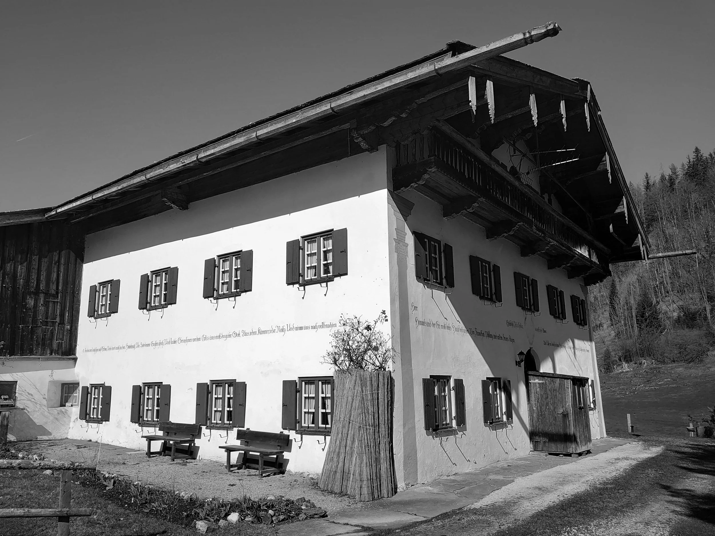 Aufnahme der Fassade eines traditionellen alpenländischen Einfirsthofs mit Klappläden, Balkon, Wandmalereien und geschnitztem Dachgebinde vor der Sanierung.