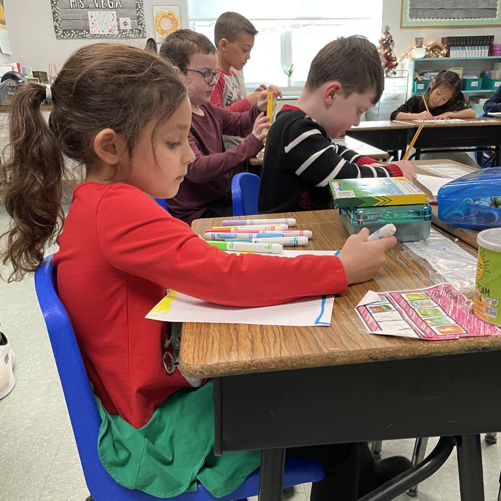 female student sitting at a desk, writing with markers