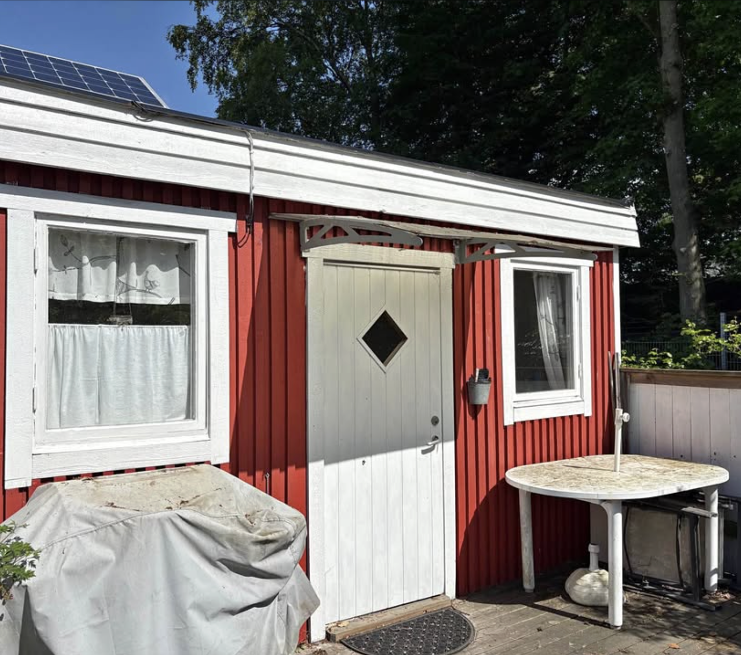Fin liten röd kolonistuga med lummig trädgård