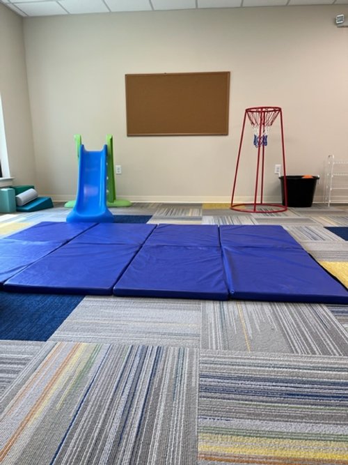 Indoor playroom with blue slide, blue gym mats, and red basketball hoop