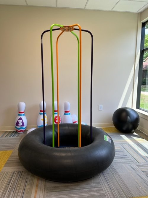 Inflatable round base with colorful rods, indoor bowling pins, and exercise ball in a room.