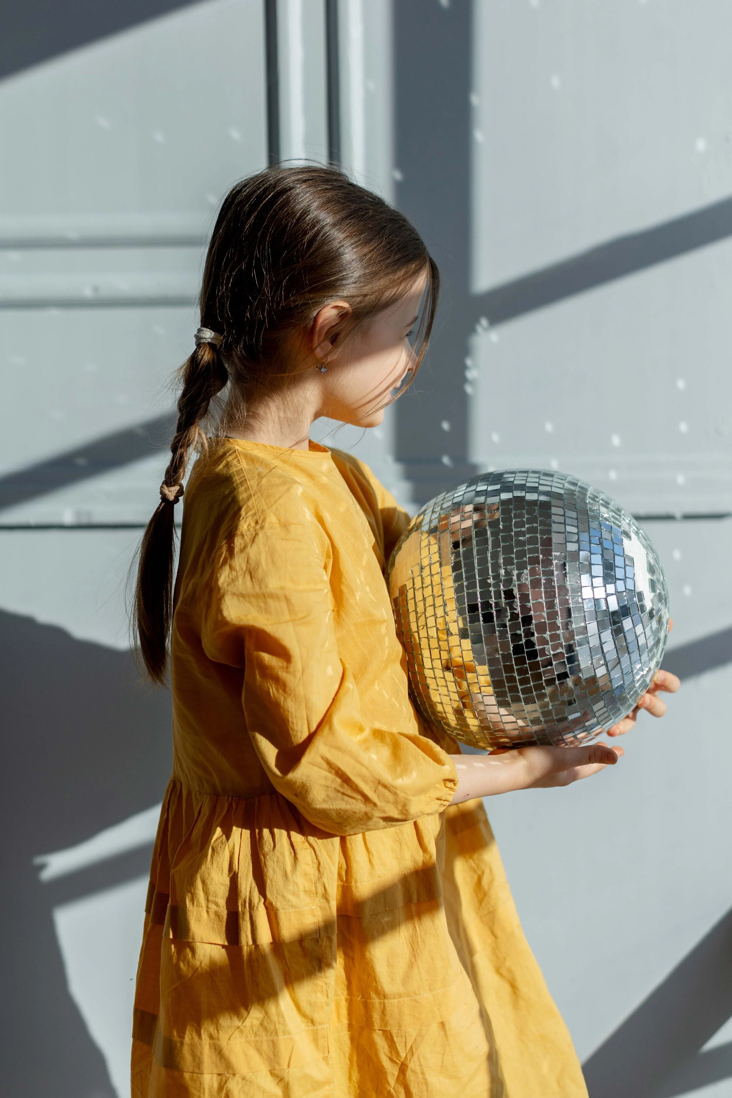 Menina com vestido de linho amarelo segurando uma bola de discoteca
