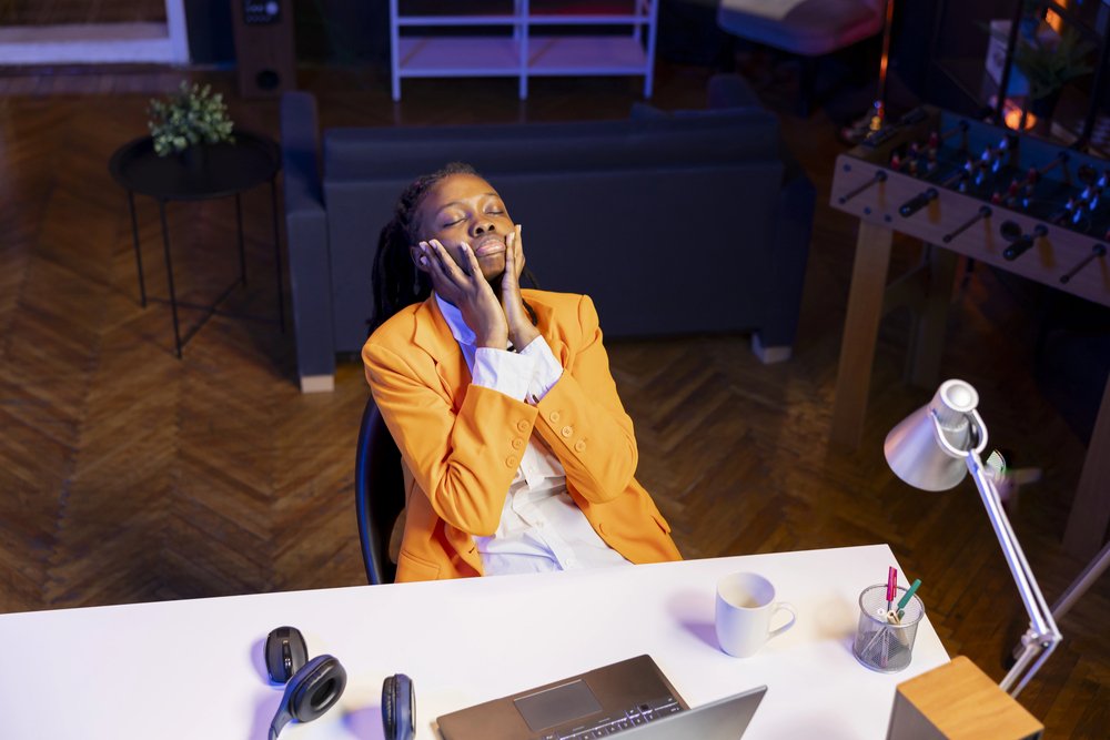 woman at her desk with her head in her hands, clearly exhausted