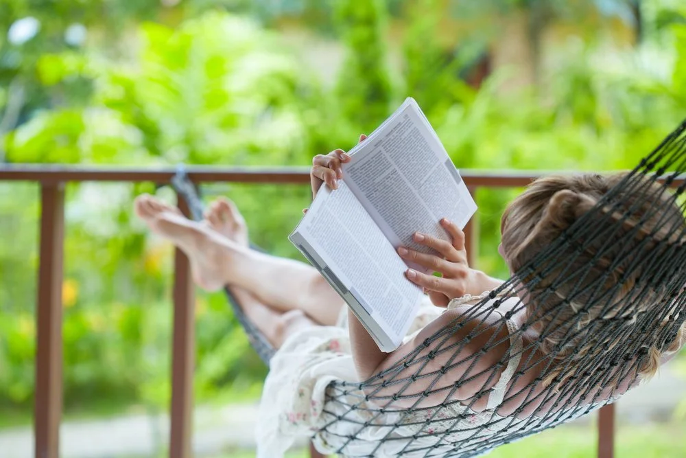 a lady lying in a hammock while reading an open book