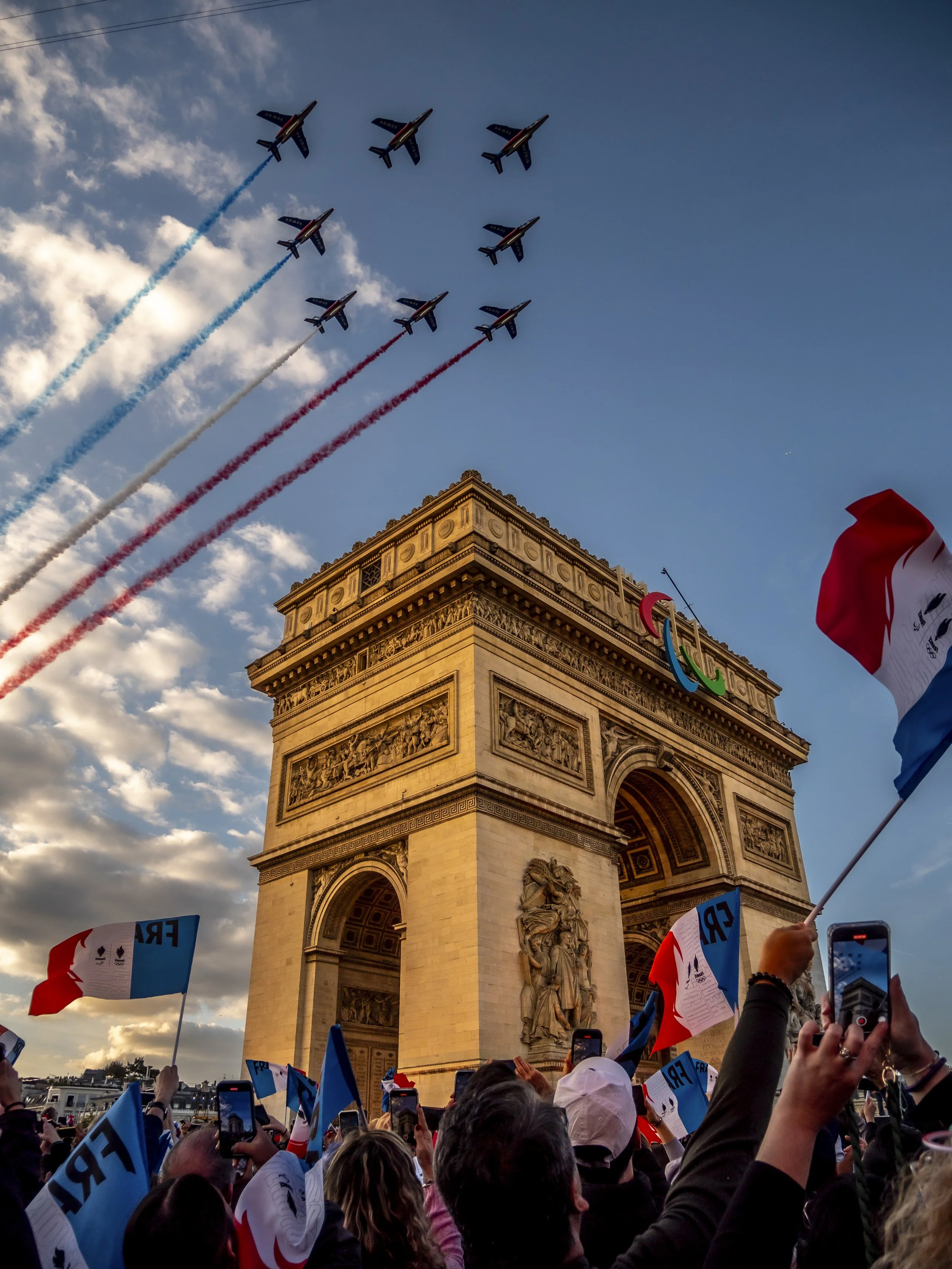 Survol de la Patrouille de France avec fumigènes tricolores au-dessus de l'Arc de Triomphe et foule en liesse lors de la parade Paris 2024 - Photo Théo Castillon