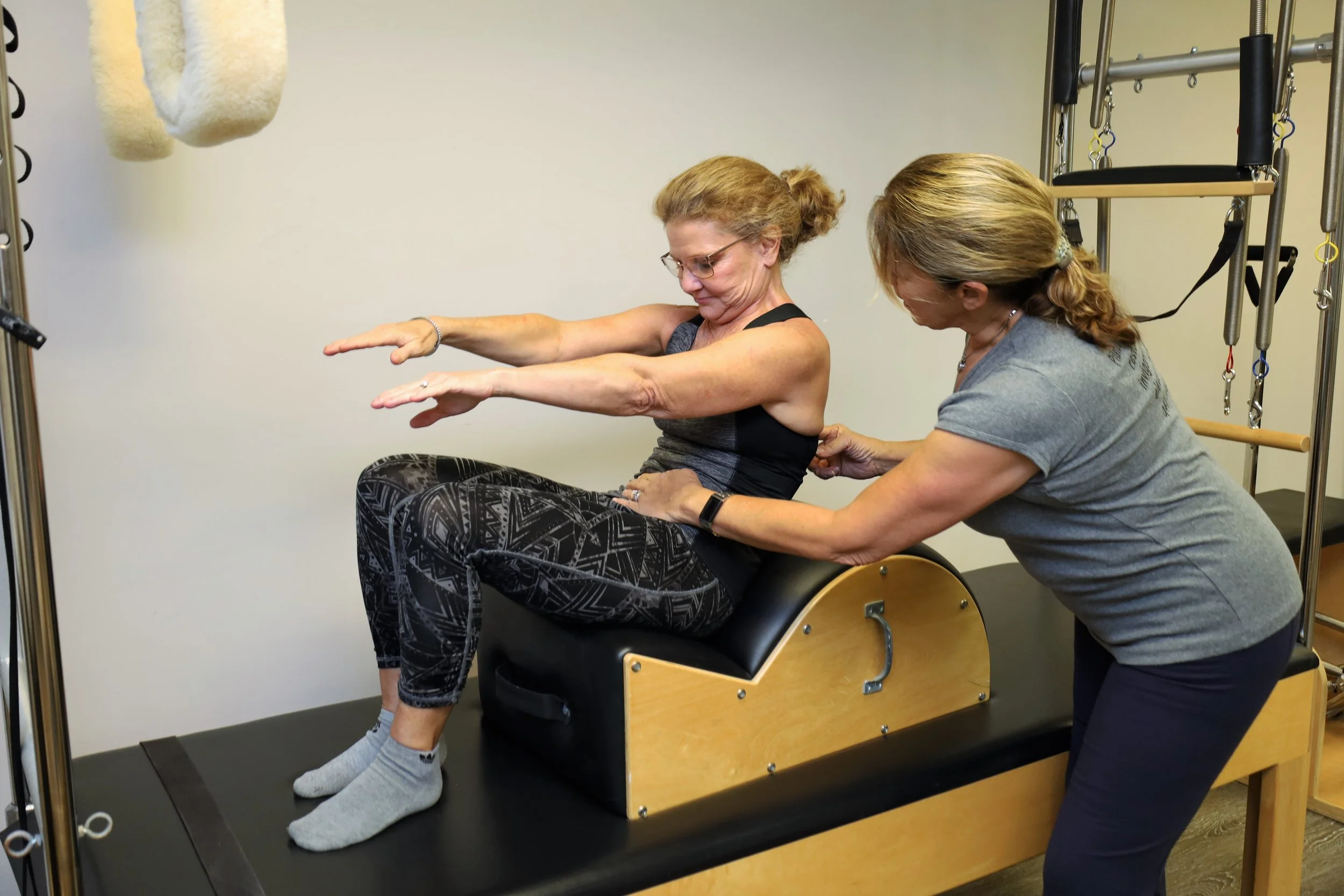 Woman on Pilates apparatus with instructor assisting