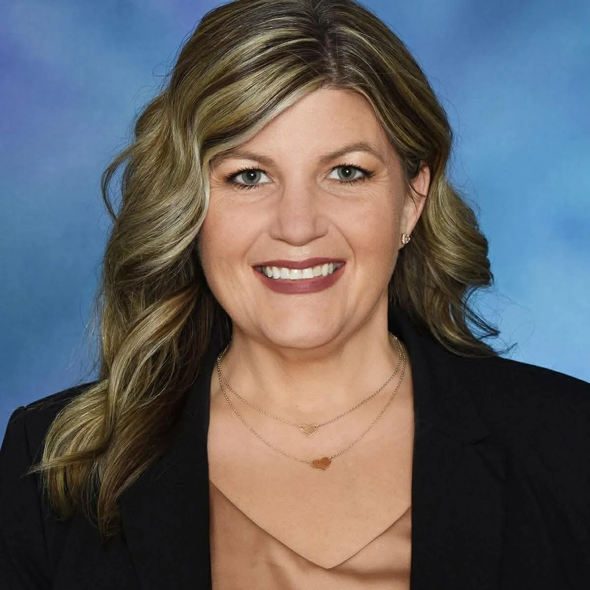 A professional woman with blonde, wavy hair posing against a blue background.