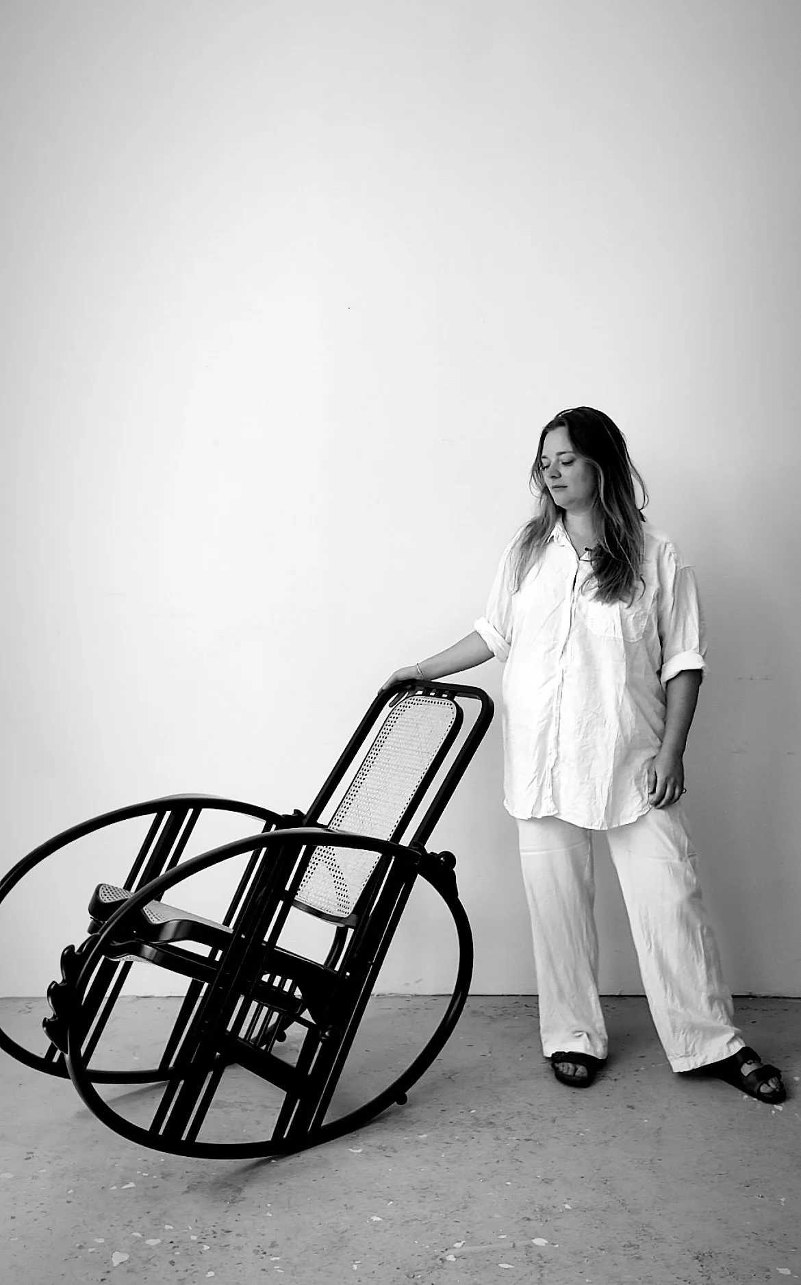 Schwarz-weißes Foto von einer Person neben einem Designer-Stuhl in einem minimalistischen Raum.