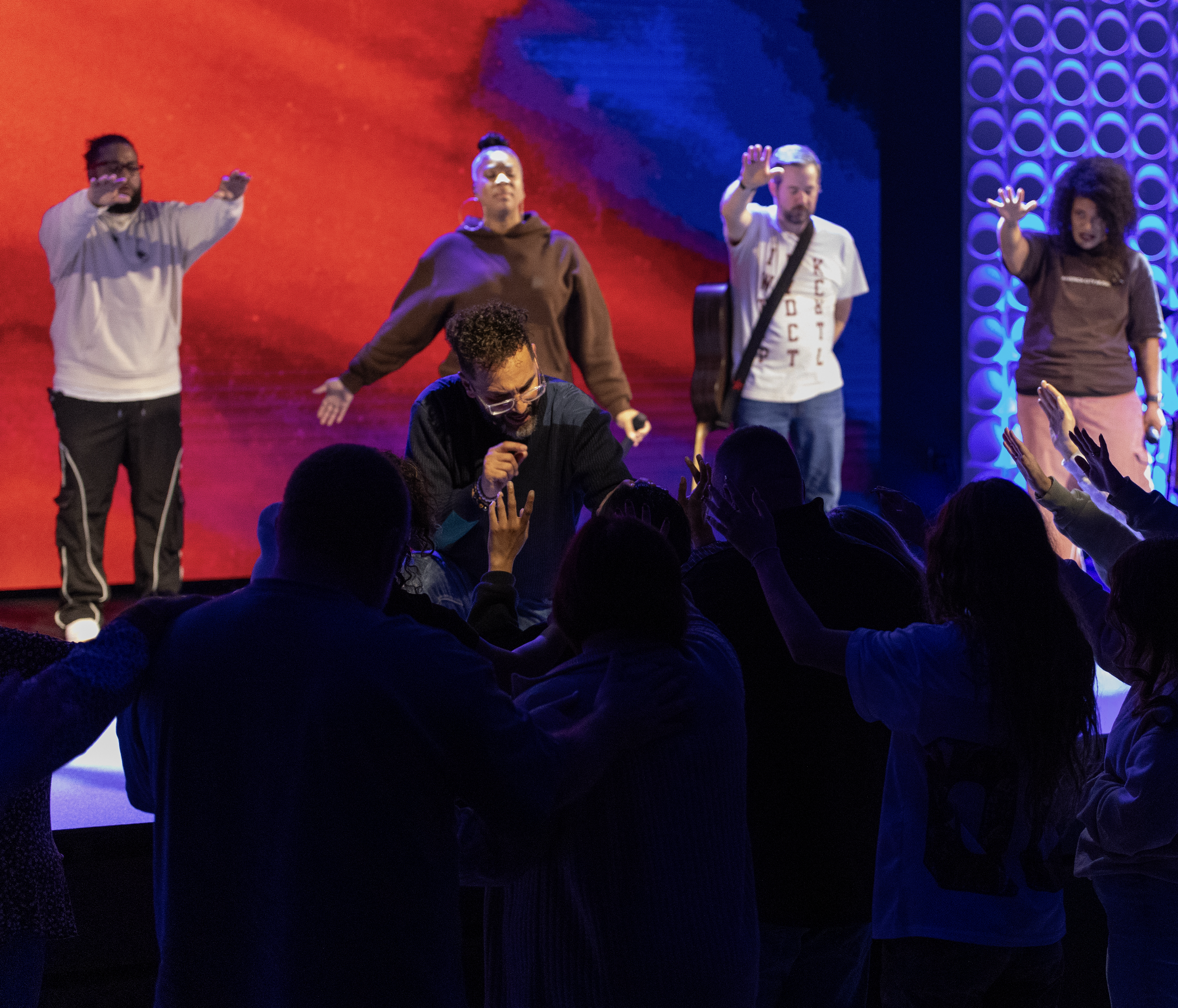 A group of people on stage with audience reaching out to them in a concert or event setting, colorful background.
