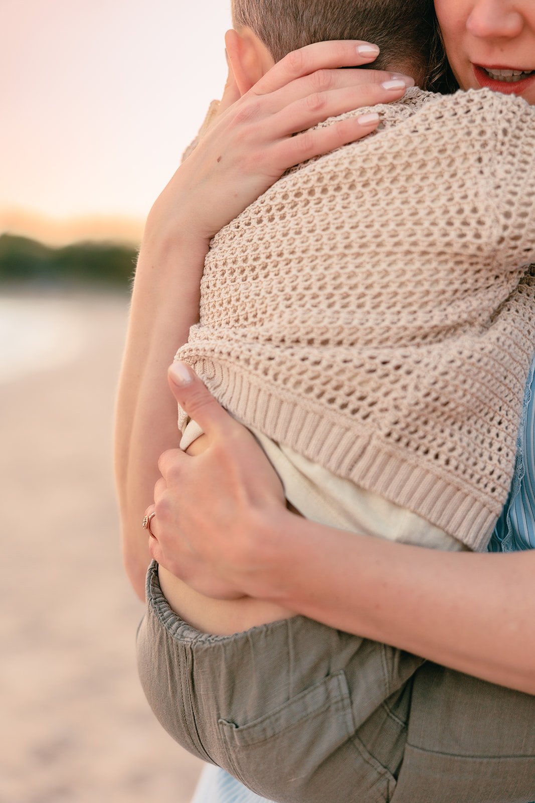 Close-up of two people hugging, with one person's face partially visible, wearing casual clothing, at the beach during sunset northport michigan