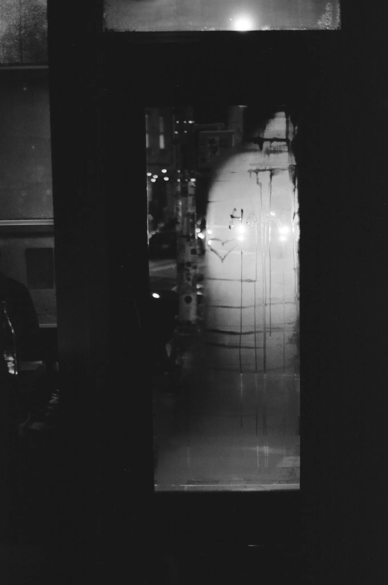 A reflective glass door with the message 'Hero' and a heart symbol drawn on it, reflecting a street scene with cars and lights at night.