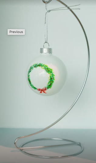 White Christmas ornament with a green wreath and red bow decoration hanging from a silver stand.