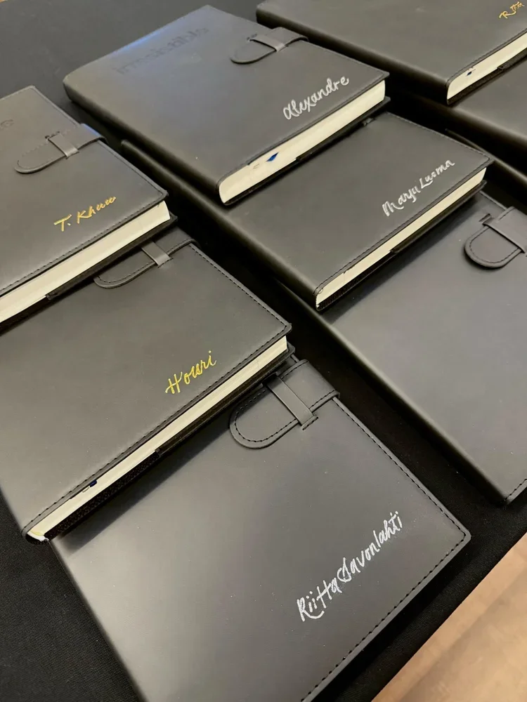 Black notebooks with gold, white, and yellow handwritten names on the covers, including T. Khuu, Alexandre, Nguyet Leu, Houri, and Keith Havadki.