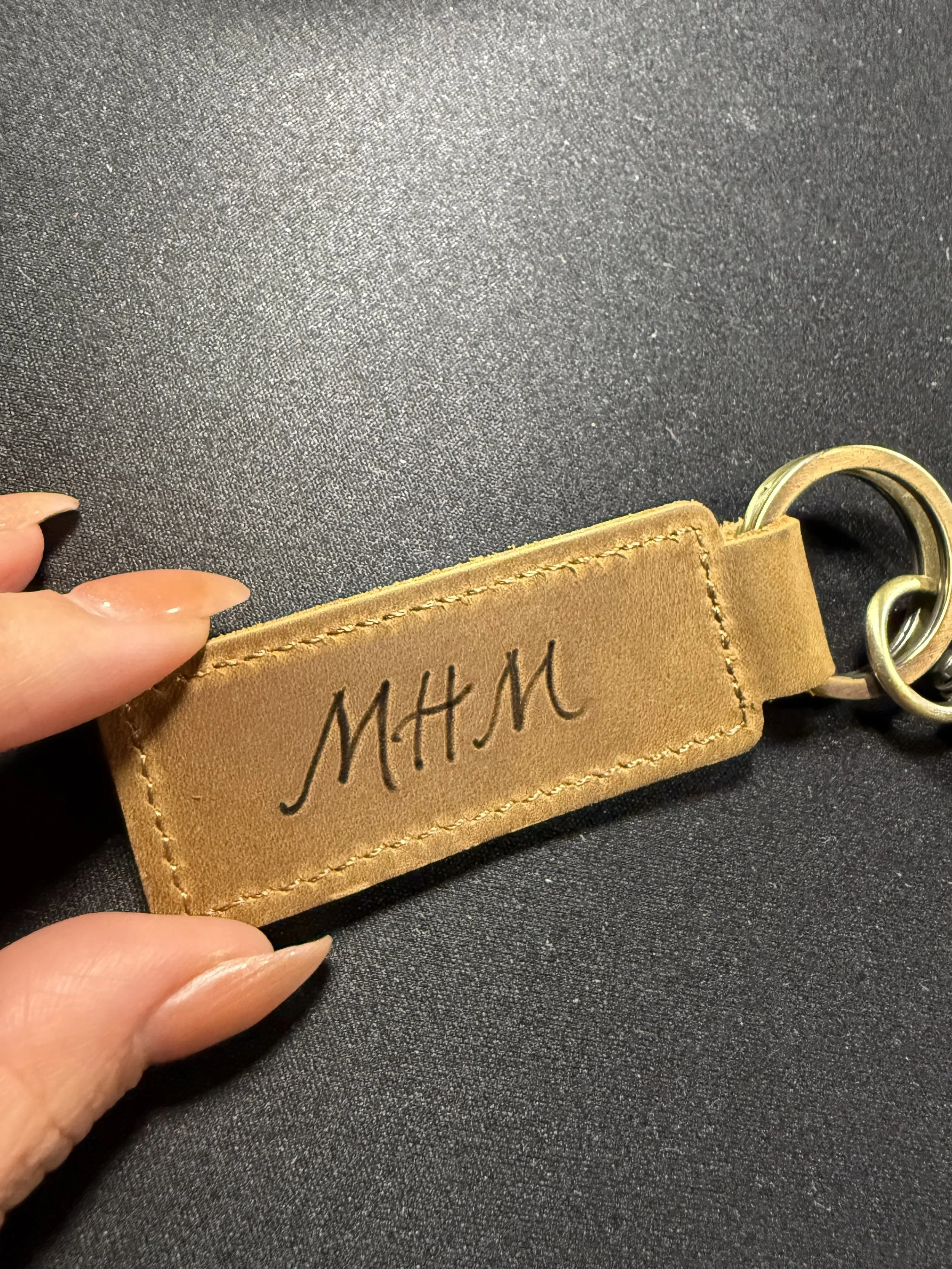 A tan leather keychain with the initials 'M.H.M' embossed on it, attached to metal rings.