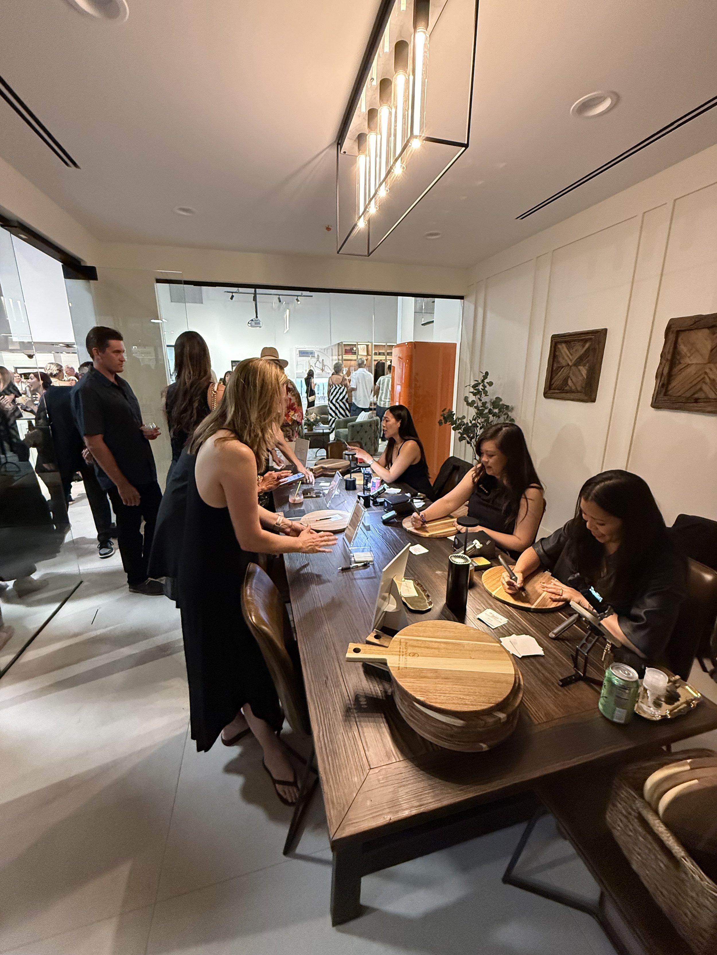 Women checking in at a hotel reception desk with a wooden tabletop and modern decor, including artwork and lighting fixtures.