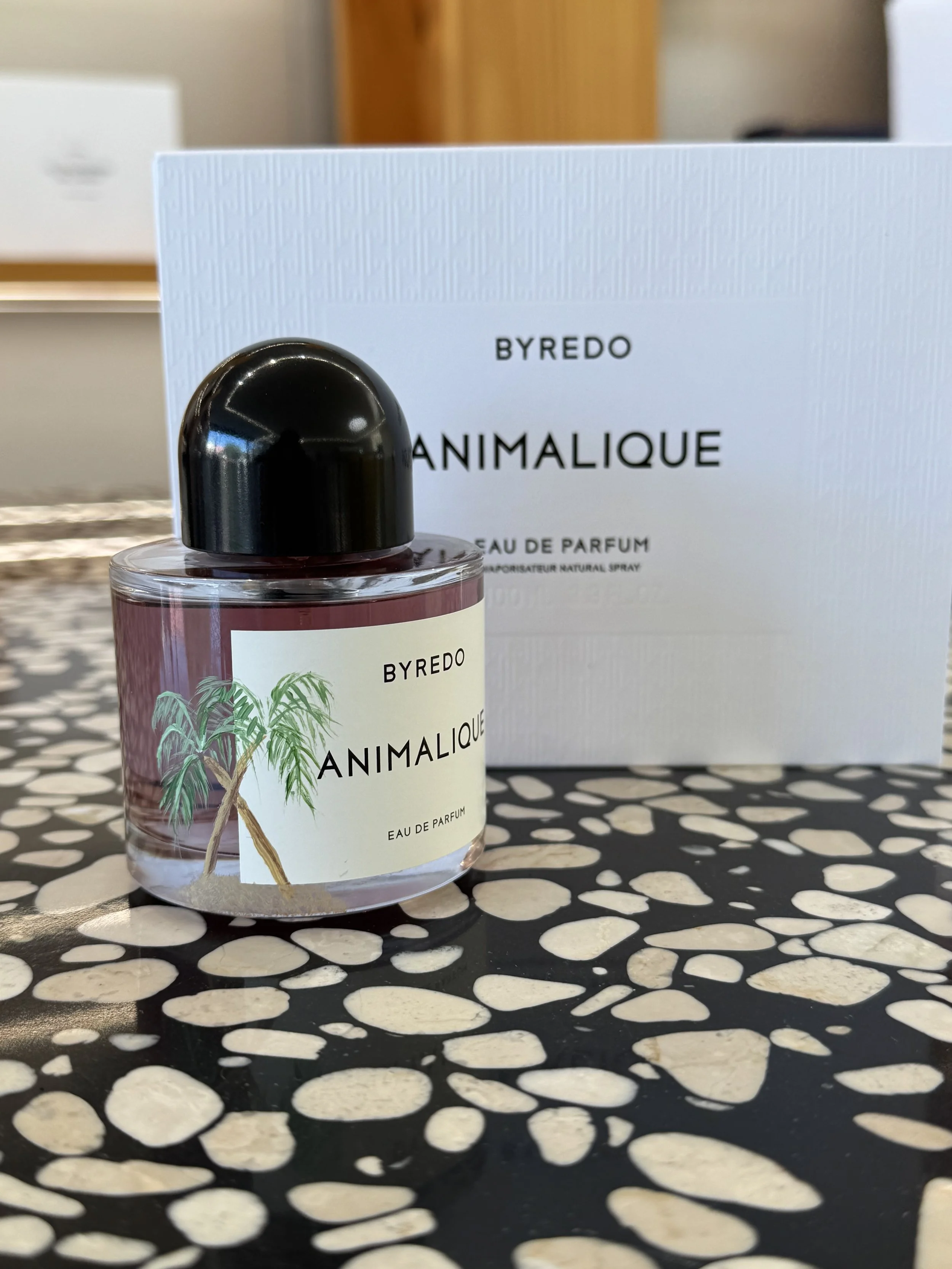 A bottle of Byredo Animalique Eau de Parfum in front of a white box, placed on a black and white speckled surface.