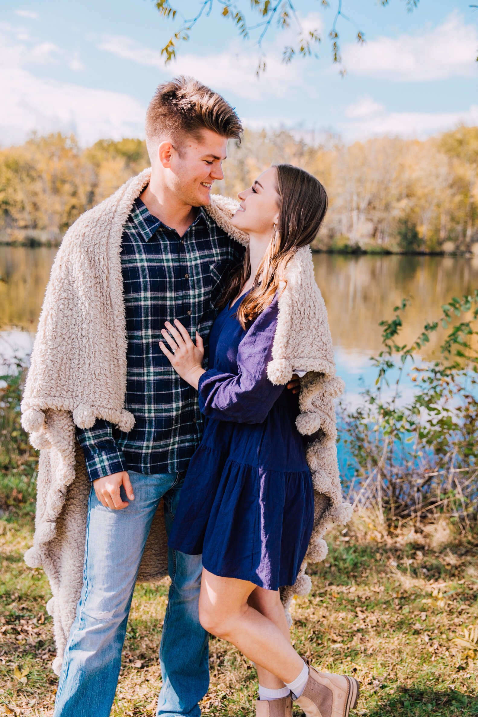  engaged couple smile at each other while cuddled up with a blanket during fall mini sessions 