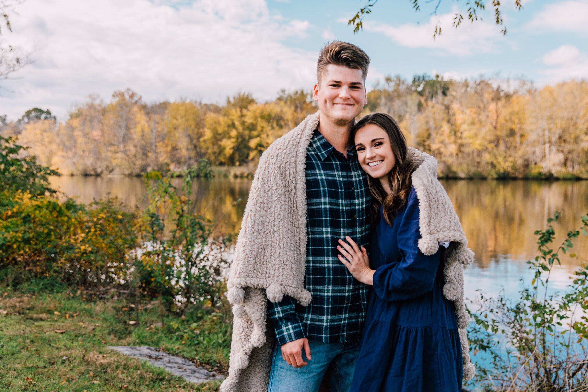  newly engaged couple stand smiling while cuddled up with a blanket in an upstate NY photographer session 