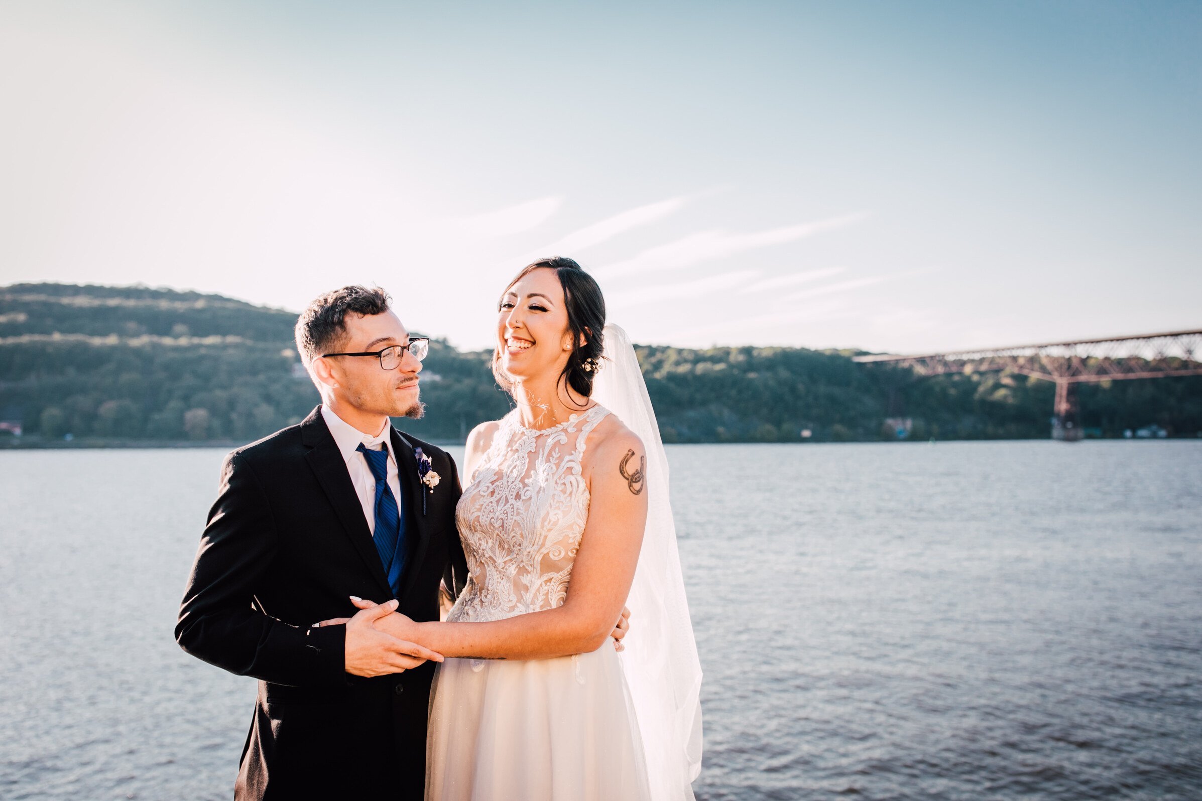  the couple smile while standing in front of the hudson at their hudson river wedding 