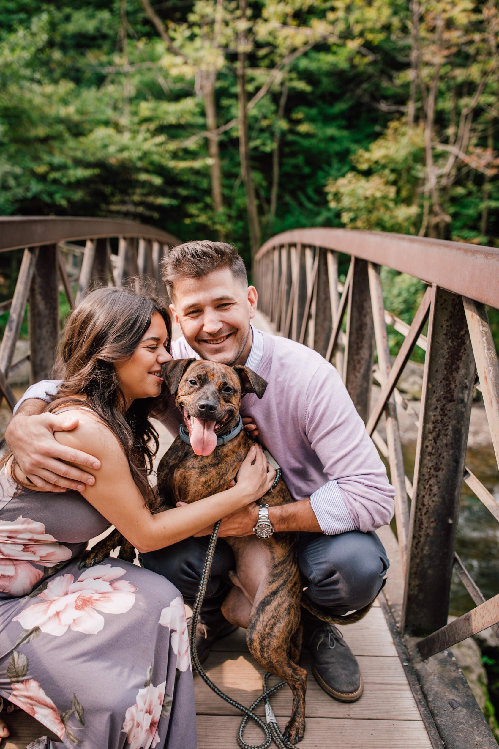 Engaged couple squat down on a bridge with their dog, dog engagement photos 