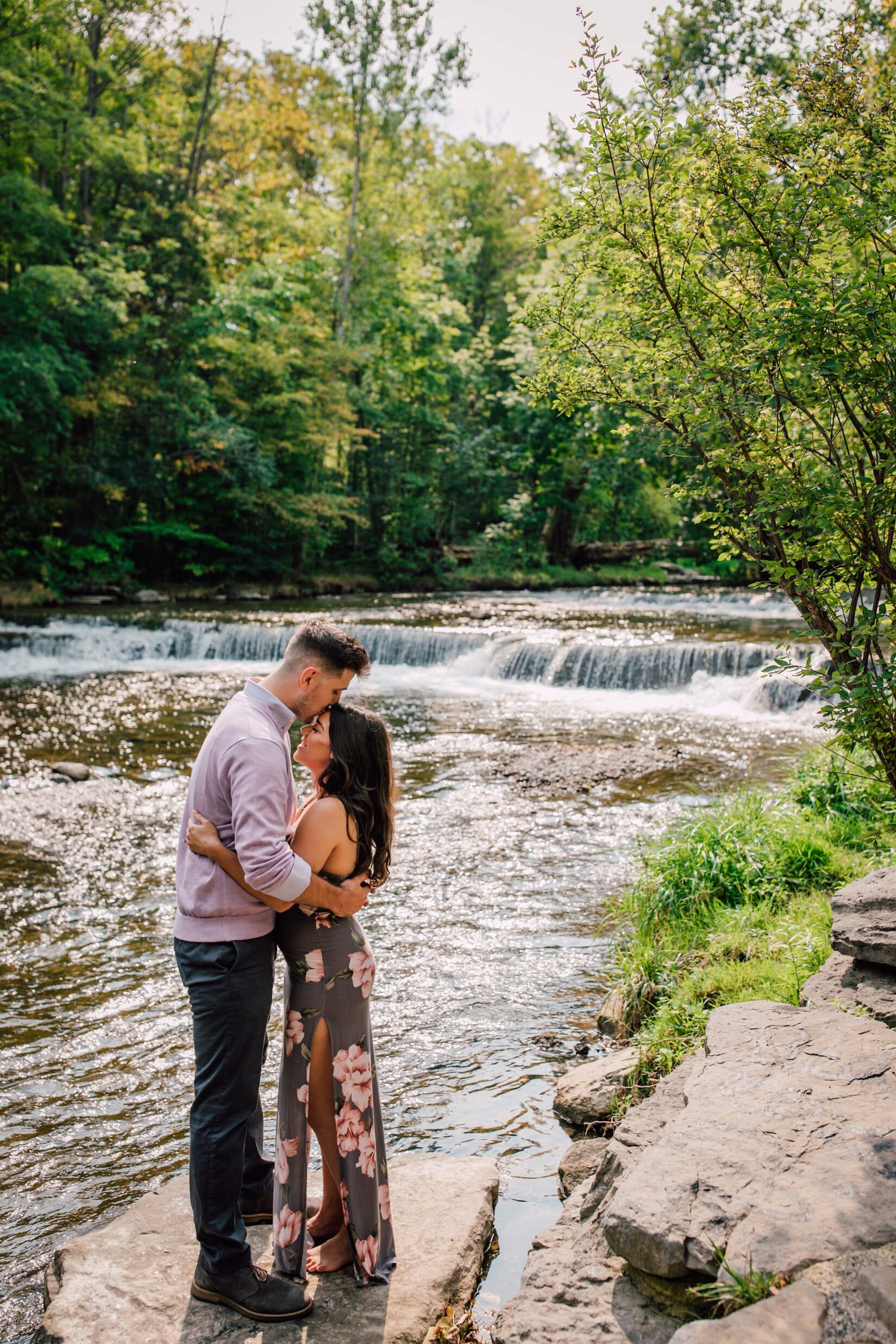  Man kisses his fiancé’s forehead in front of a waterfall, waterfall engagement photos 