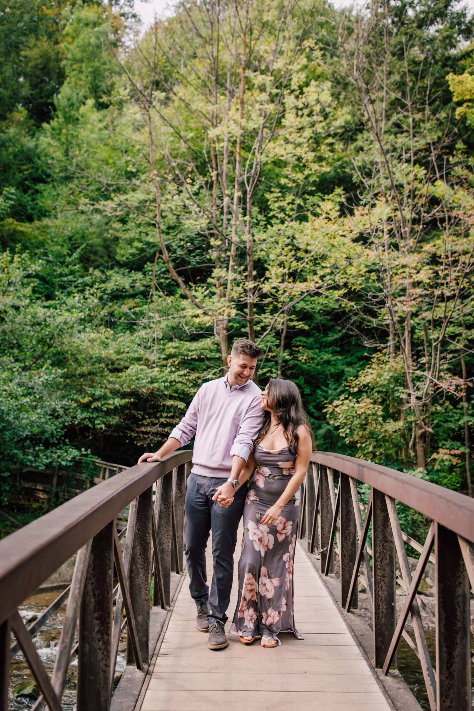  Engaged couple smile at each other as they walk over a bridge, chittenango falls 
