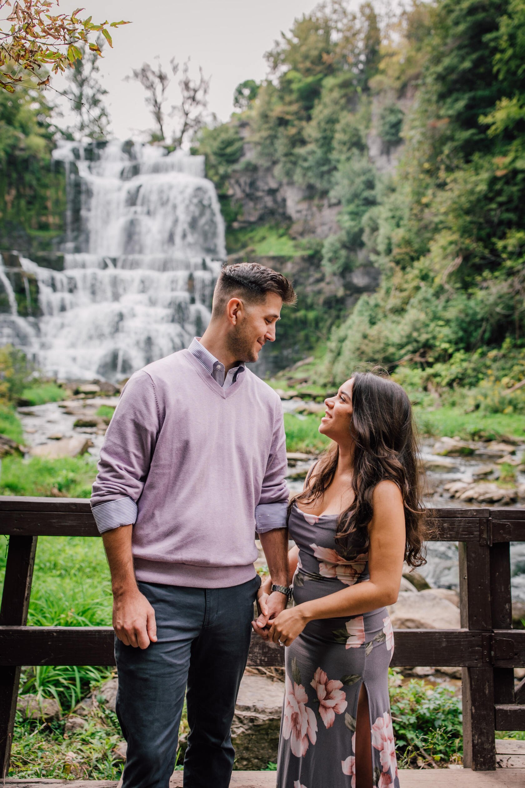  Engaged couple smile at each other as they stand in front of chittenango falls, waterfall engagement photos 