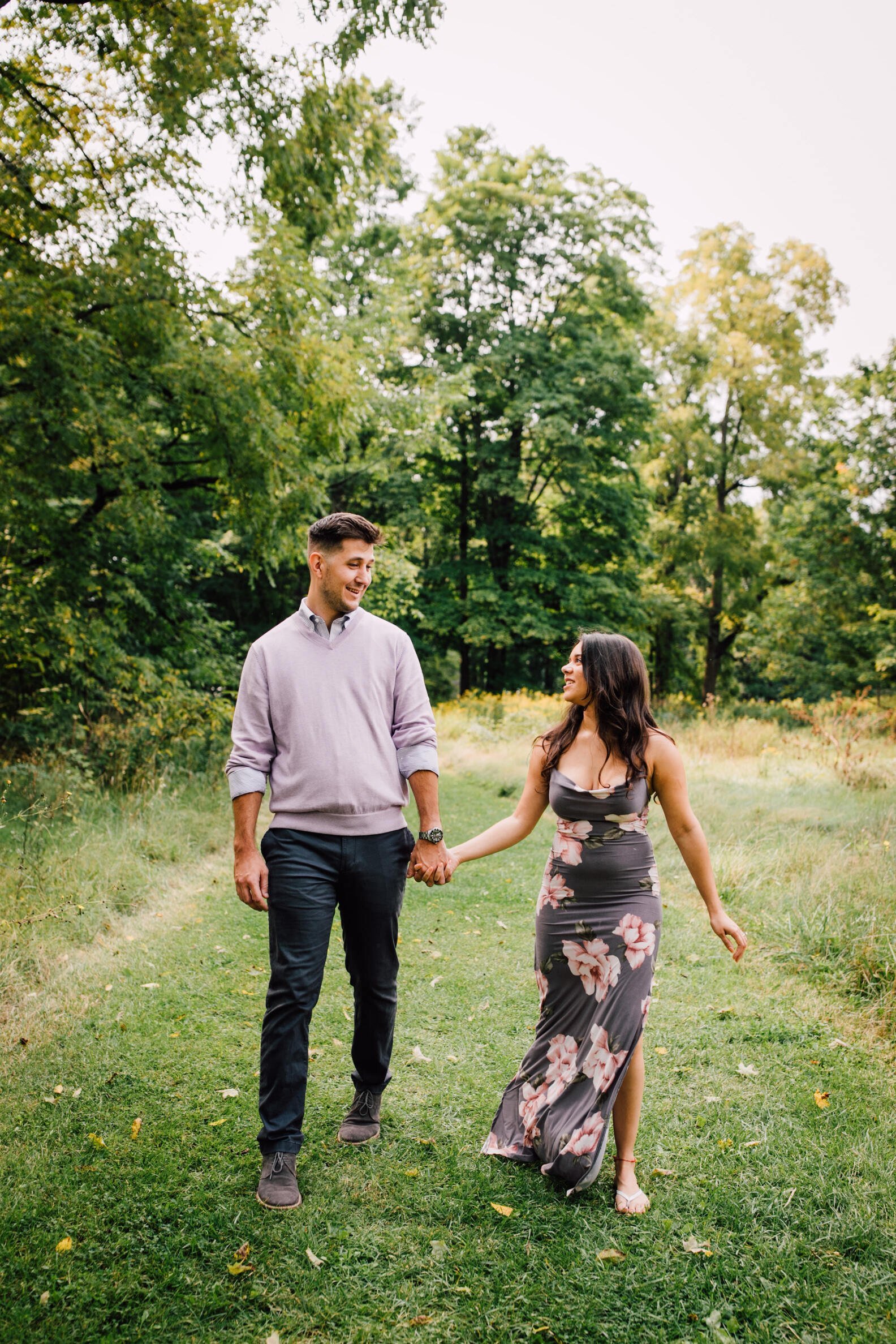  Engaged couple smile as they walk together through a grassy area at chittenango falls, syracuse, ny 