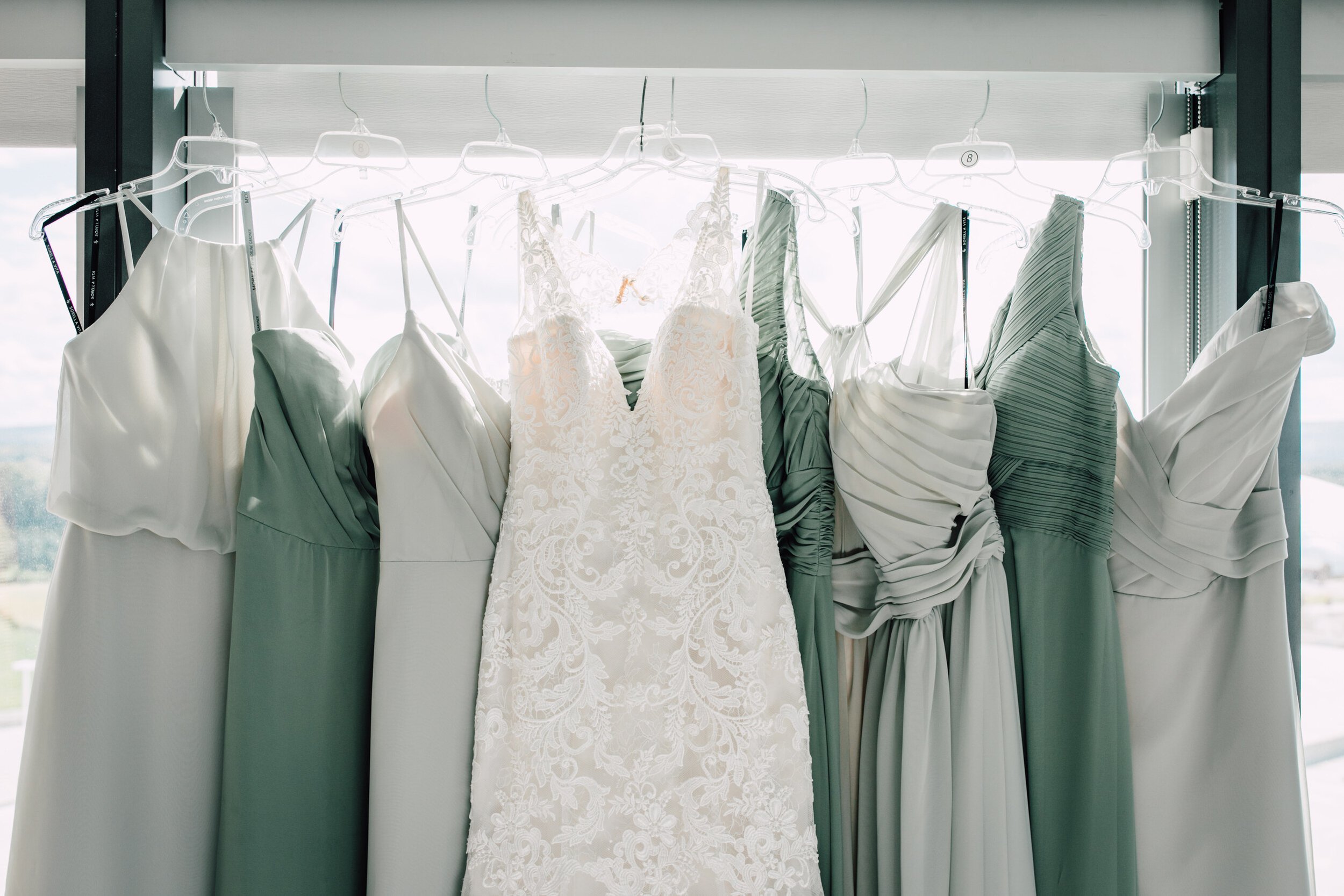  Mint and sage green bridesmaids dresses hang to the sides of a wedding dress 