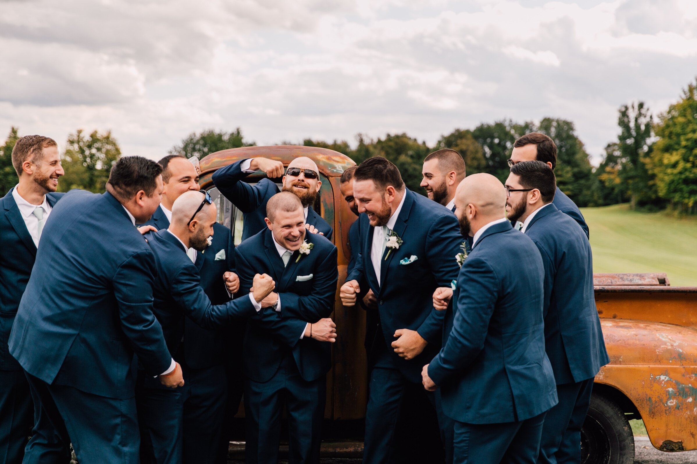  The groom and groomsmen stand in front of a vintage truck as the groomsmen laugh and pump up the groom&nbsp; 