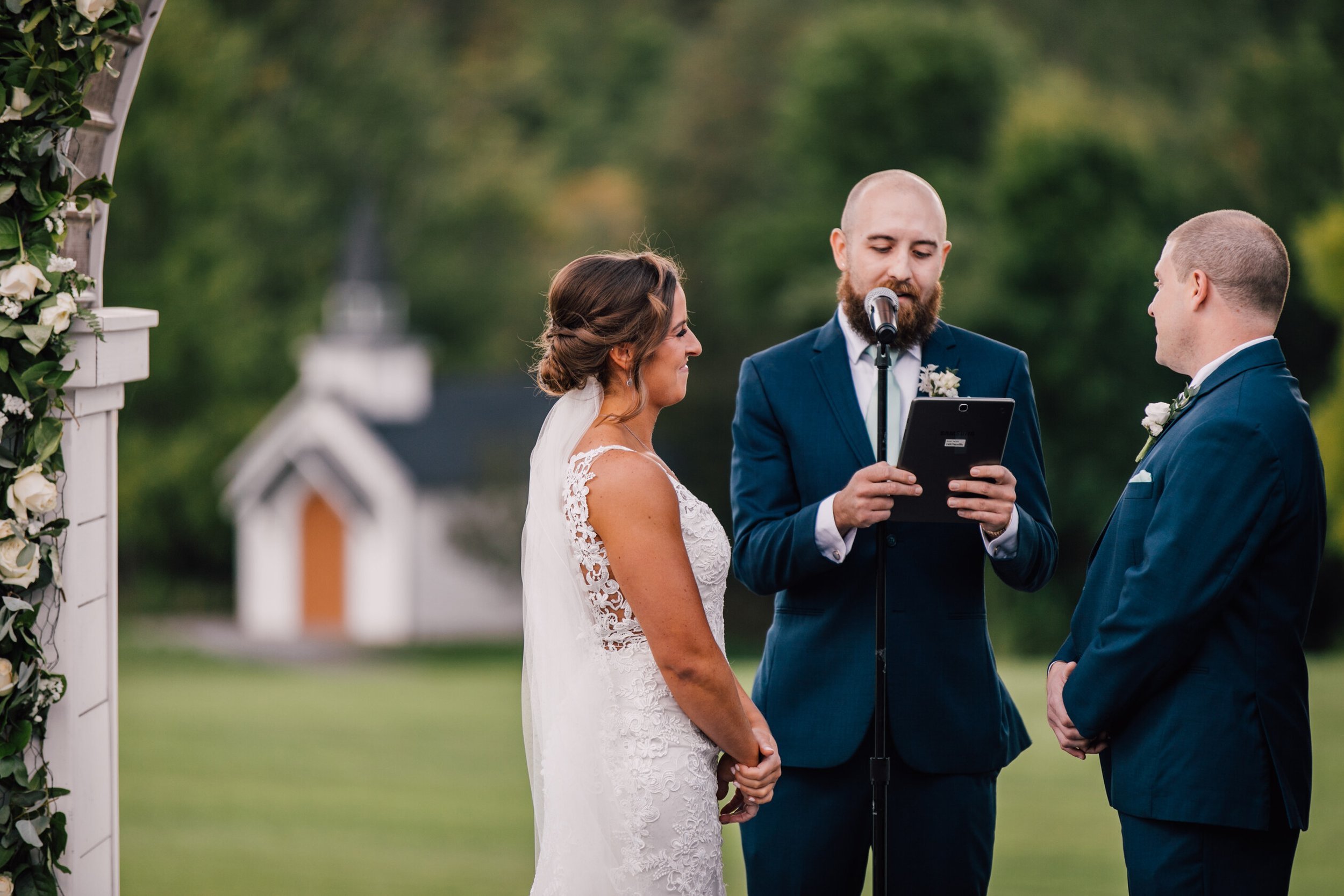  The bride and groom smile as their officiant reads between them during their ceremony 
