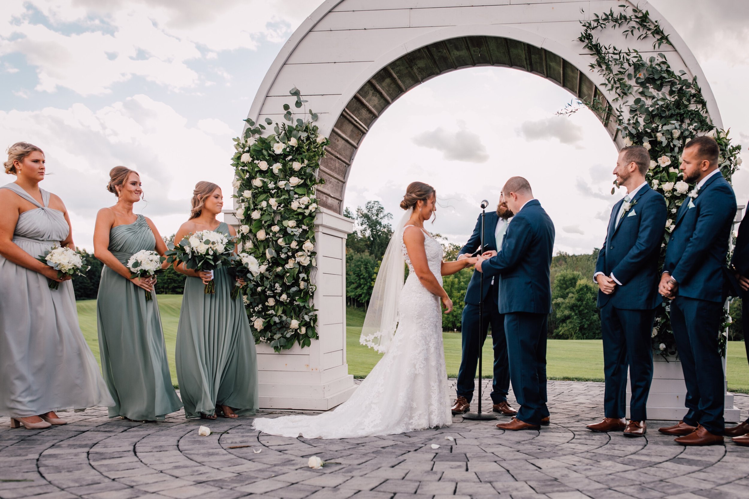  The groom places a ring on the brides finger under the wooden wedding arch 
