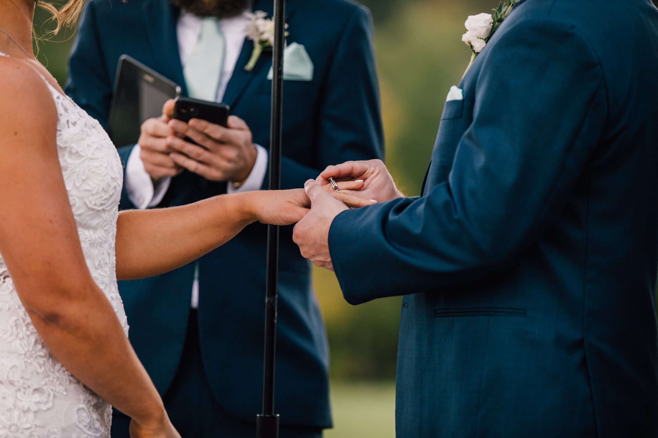  A closeup of the groom placing a ring on the bride’s finger during their rustic barn wedding 