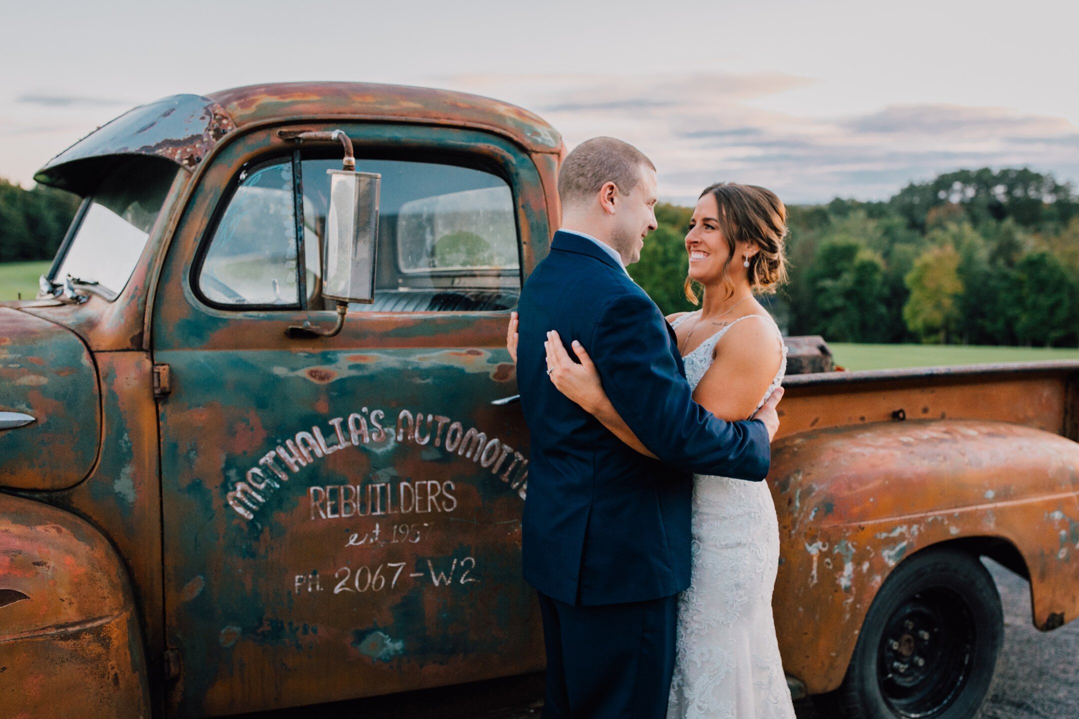  The bride and groom stand in front of a vintage truck during their rustic barn wedding 
