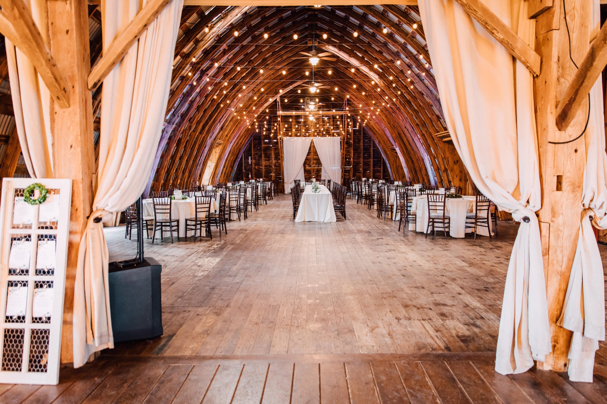  A view from the entrance of the wedding venue set up with tables, chairs, and barn wedding decor 