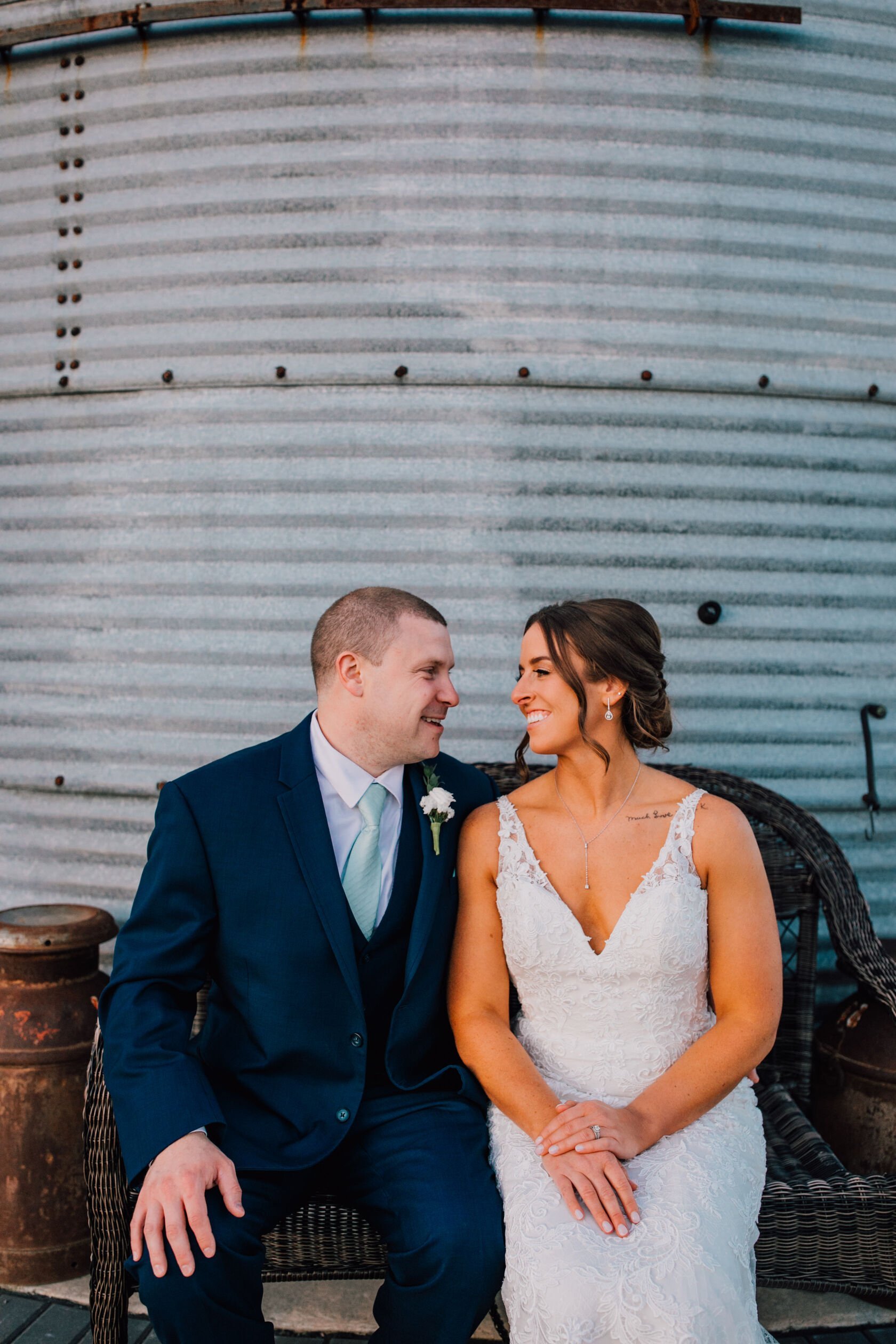  The bride and groom sit on a bench in front of a silo at their barn wedding 