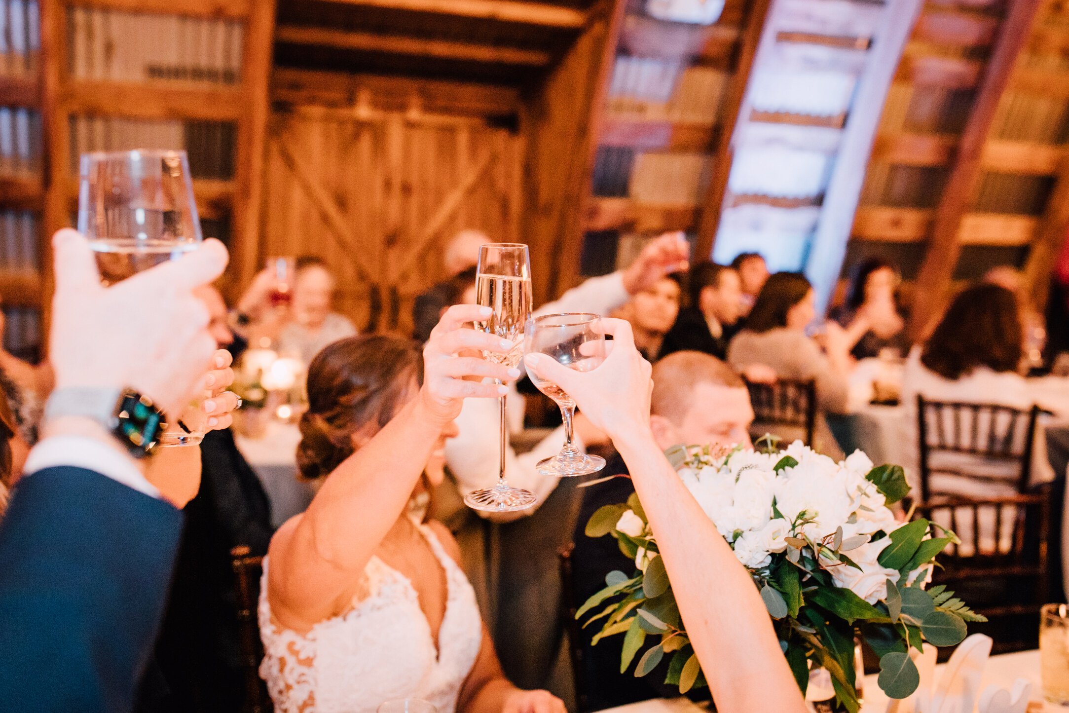  The bride, groom, and guests raise a glass as they listen to toasts at their barn wedding 