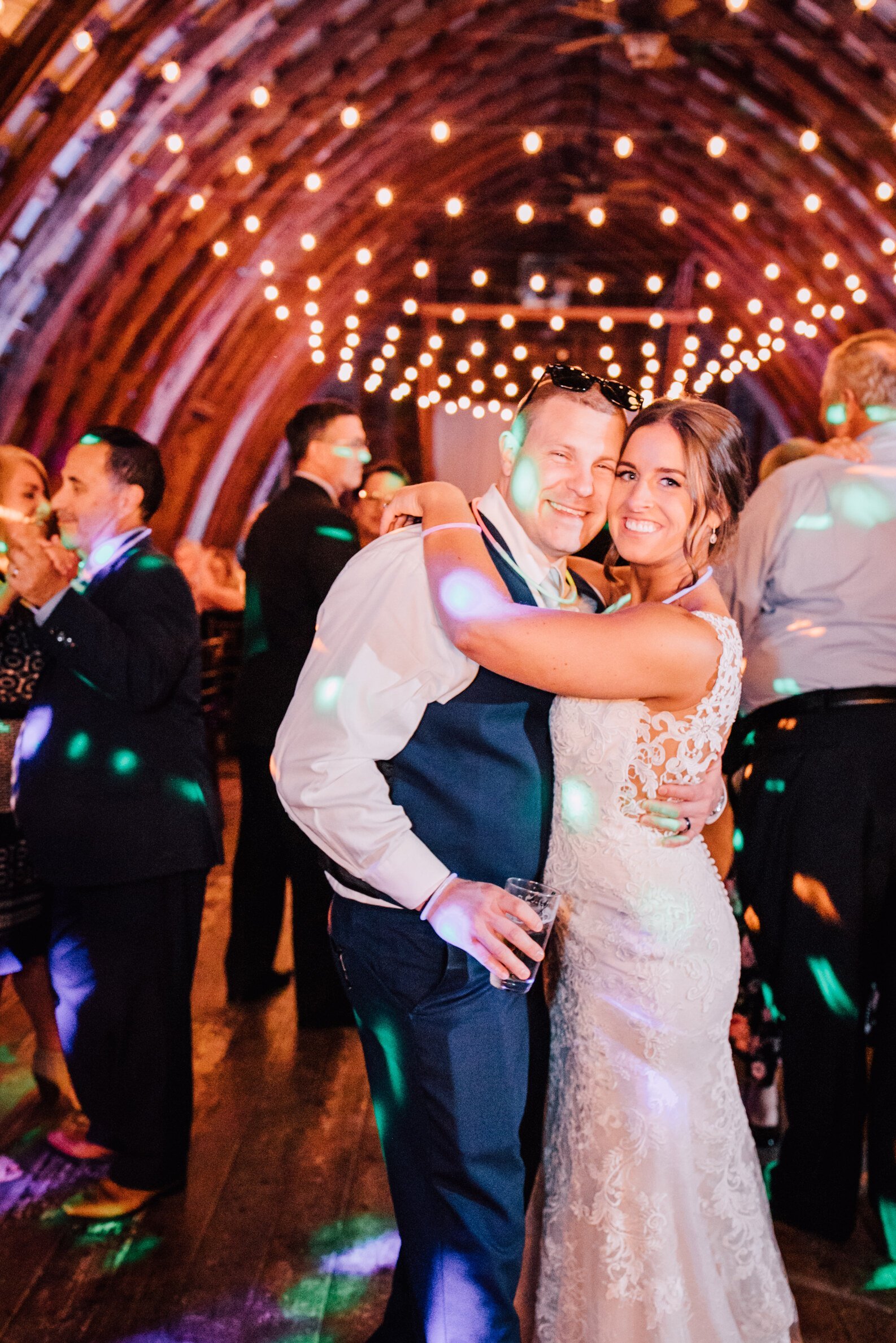  The bride and groom smile from the dance floor of their hayloft on the arch wedding reception 