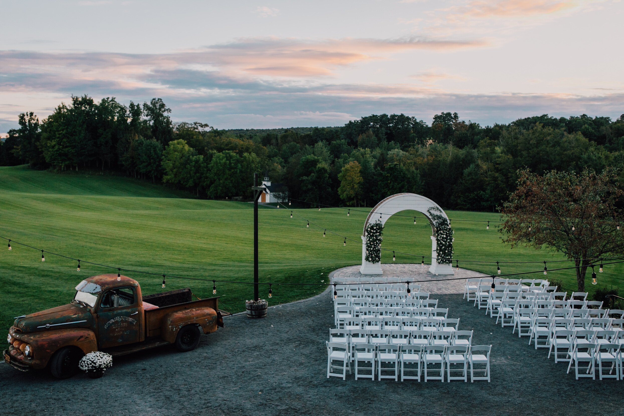  A view of the wood wedding arch and vintage truck in front of a field at hayloft on the arch at sunset 