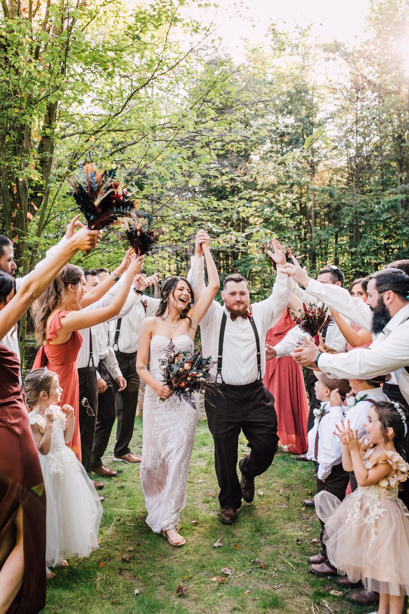  The bride and groom throw their arms in the air as they are surrounded my their wedding party cheering for them after their outdoor fall wedding 