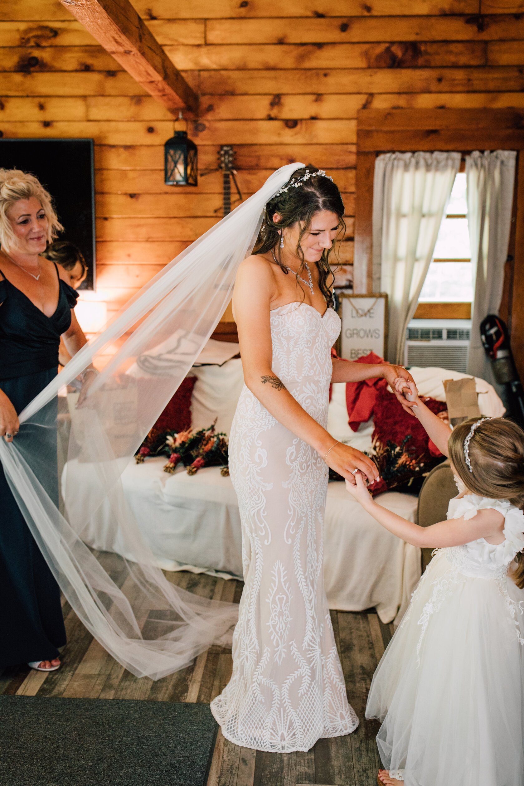  The bride stands smiling at her daughter while holding her hands as her mother adjusts her veil before her rustic wedding 