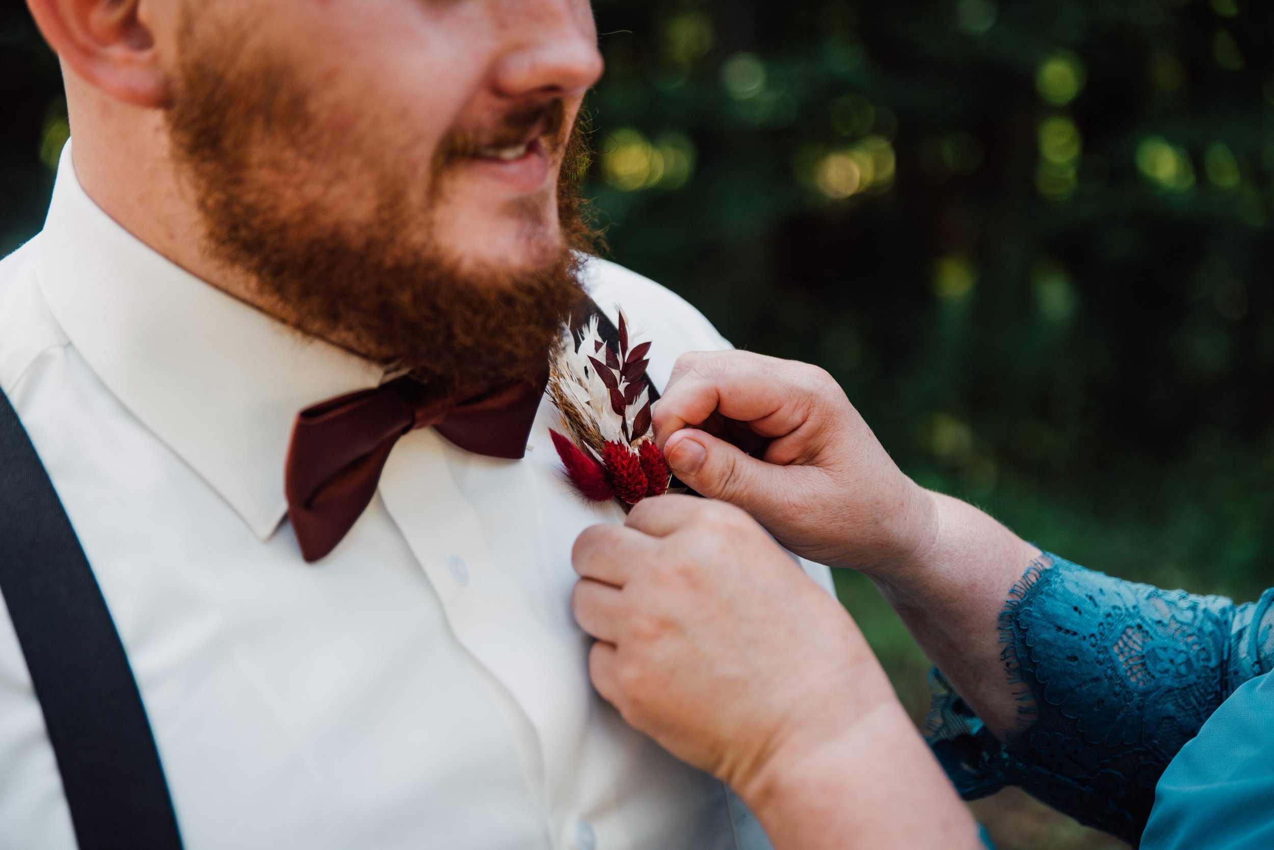  The groom’s mom pins his boutonniere to his shirt before his outdoor fall wedding 
